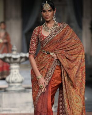 Model in ornate Indian saree showcases elegance during a high fashion runway event.
