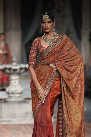 Model in ornate Indian saree showcases elegance during a high fashion runway event.
