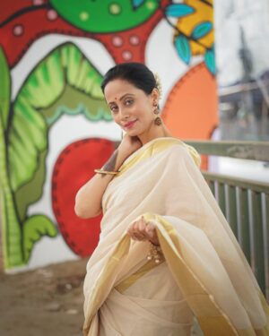 Elegant woman in a saree posing outdoors with a colorful mural backdrop.