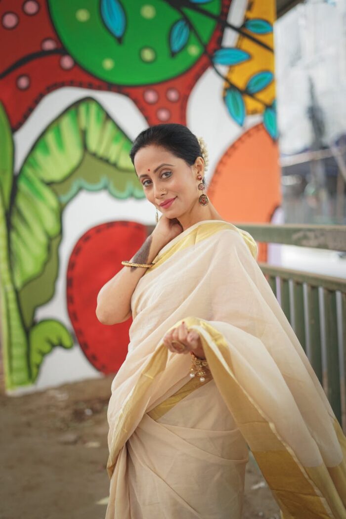 Elegant woman in a saree posing outdoors with a colorful mural backdrop.